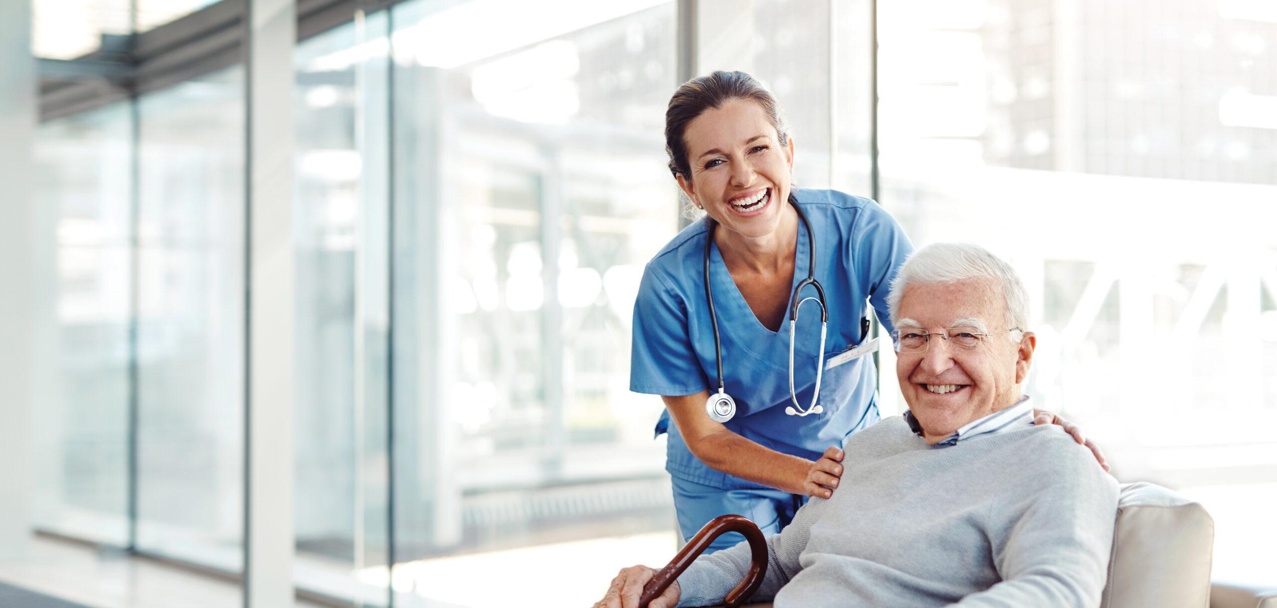 A healthcare worker smiles with an older man, who is seated.